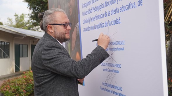 Fotografía del Rector Helberth Choachí, firmando cartel simbólico del convenio de fortalecimiento de la infraestructura y la oferta educativa.